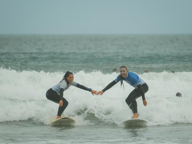 Two surfers riding a wave in together, hands held