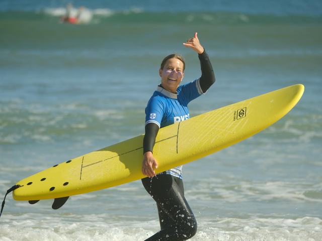 A surfer walking back up the beach grinning, board under her arm