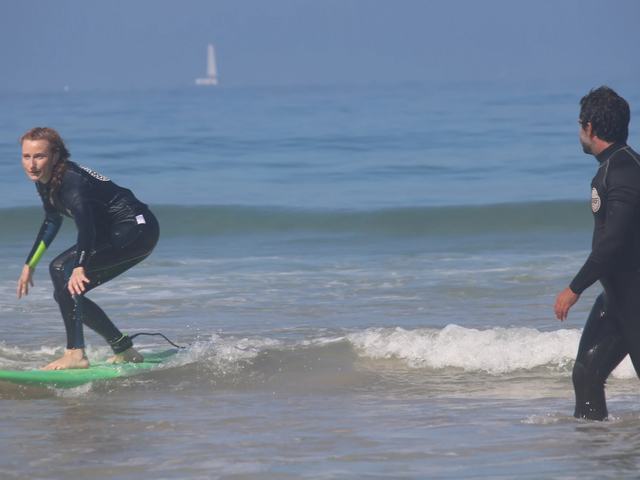 A student riding the whitewater with her coach watching from the water