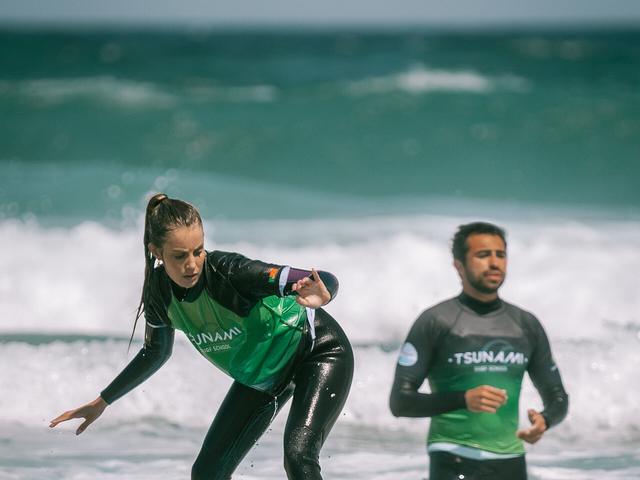A student riding a wave with her coach alongside